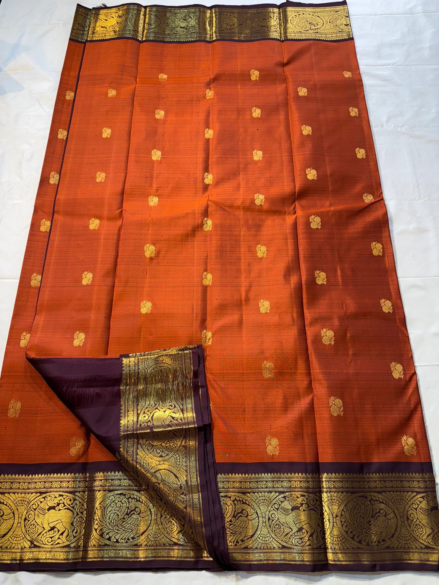 Rust Orange & Wine Korvai – Pure Kanchipuram Silk Saree
Burnt rust-orange shot body with dainty gold paisley buttas
Deep wine korvai borders in antique gold—Annapakshi & Yaali medallions
Grand wine pallu with full-zari jaal & temple panels
Silk Mark