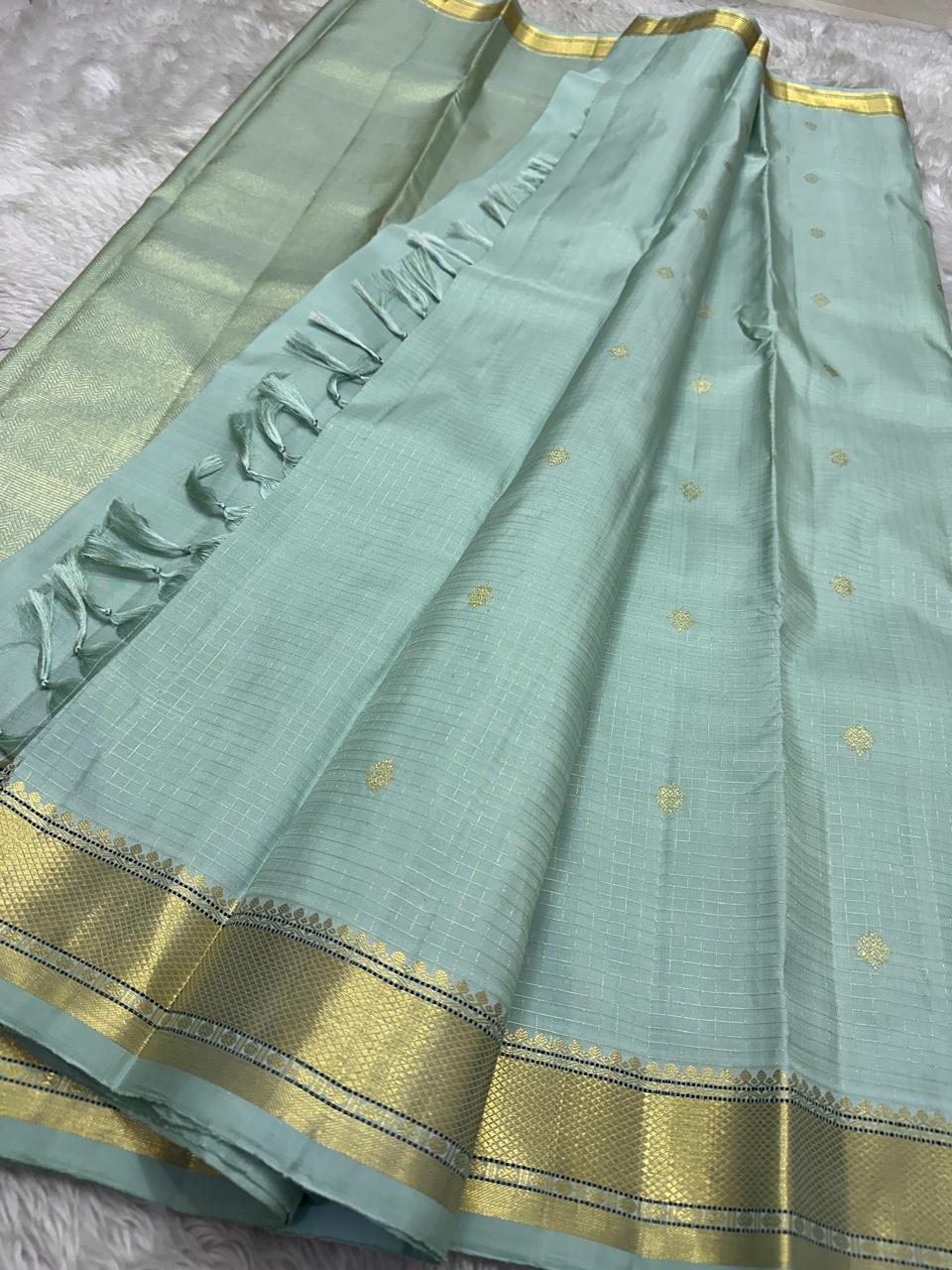Mint Kattam – Pure Kanchipuram Silk Saree
Pastel Mint Green Body with Fine Zari Checks & Buttas
Broad Gold Zari Border with Textured Tissue Weave
Rich Gold Zari Pallu in Chevron & Striped Bands
Silk Mark Certified, delivery in 2 weeks