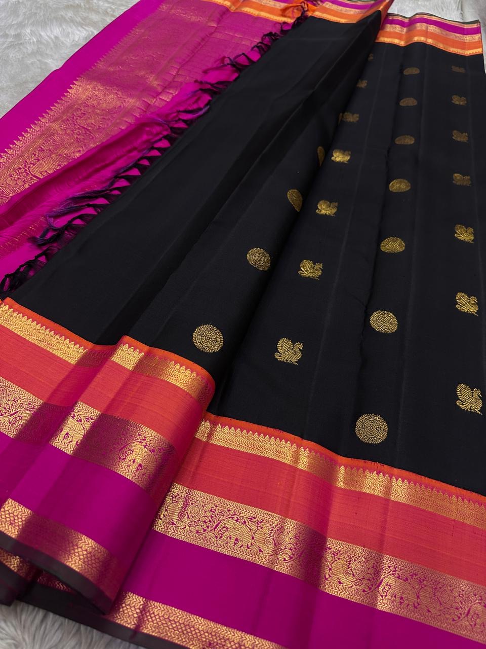 Kanmani — Black & Rani Pure Silk Kanchipuram Saree
Inky black body with gold medallion & peacock buttas
Striking rani-pink and kavi-orange korvai borders with temple-edge zari
Rich rani-pink brocade pallu with grid jaal & heritage vines
Silk Mark Cert