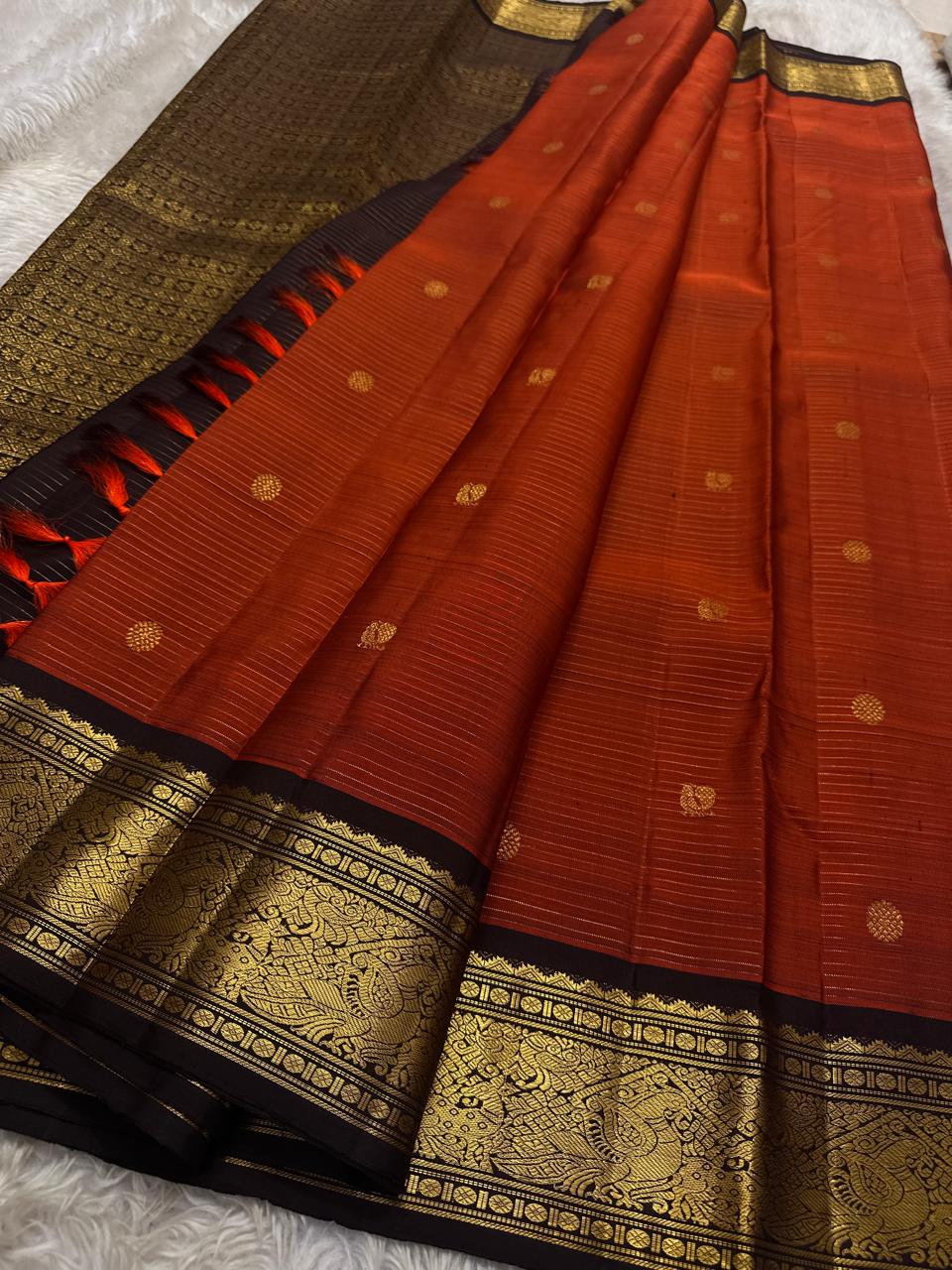 Amber Plume – Pure Kanchipuram Silk Saree
Amber Burnt-Orange Body with Vaira Oosi Stripes
Rudhraksham & Mayil Zari Woven Buttas All Over
Contrast Coffee-Brown Border with Peacock Motif Panel
Silk Mark Certified, delivery in 2 weeks