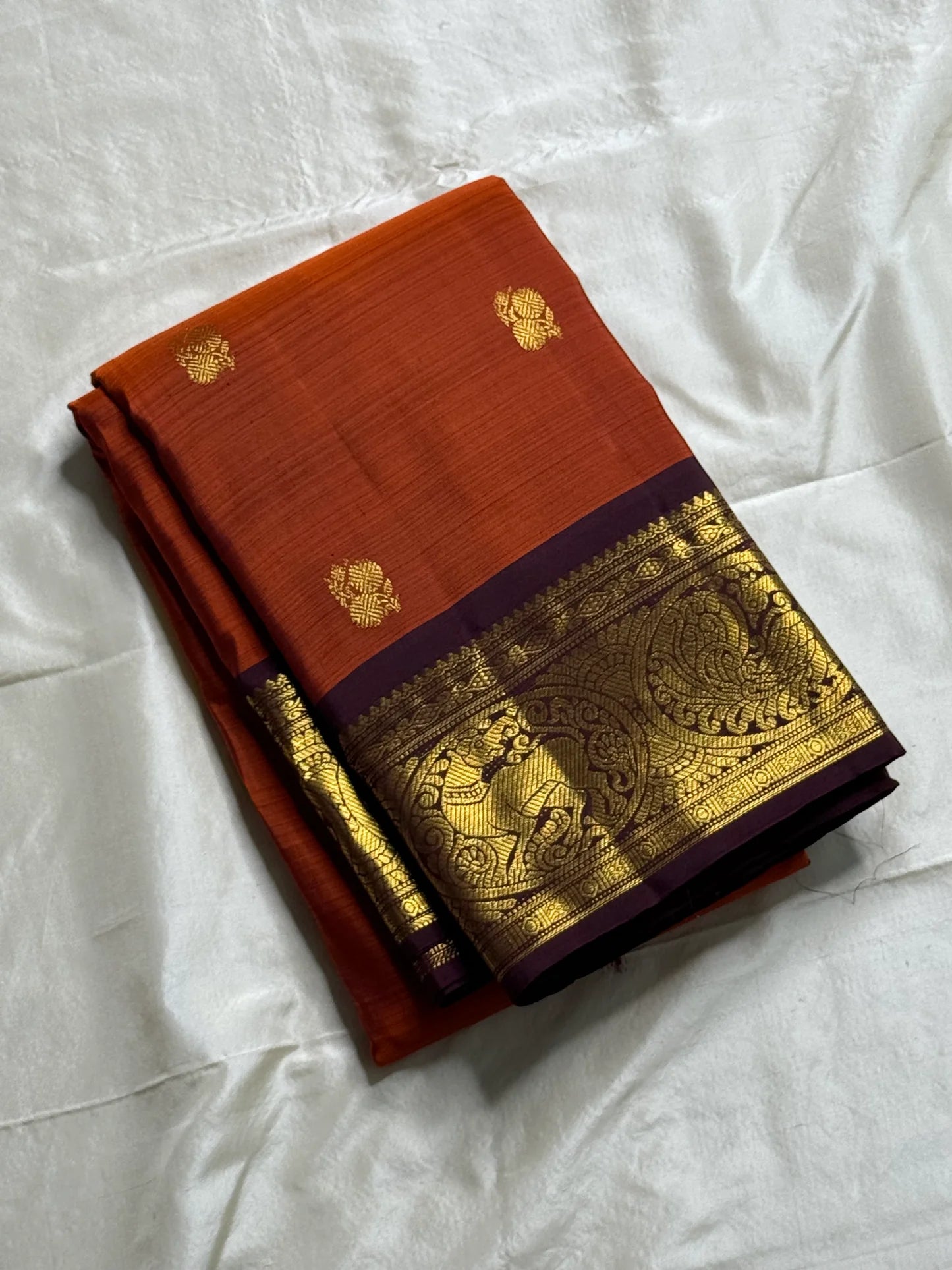Rust Orange & Wine Korvai – Pure Kanchipuram Silk Saree
Burnt rust-orange shot body with dainty gold paisley buttas
Deep wine korvai borders in antique gold—Annapakshi & Yaali medallions
Grand wine pallu with full-zari jaal & temple panels
Silk Mark