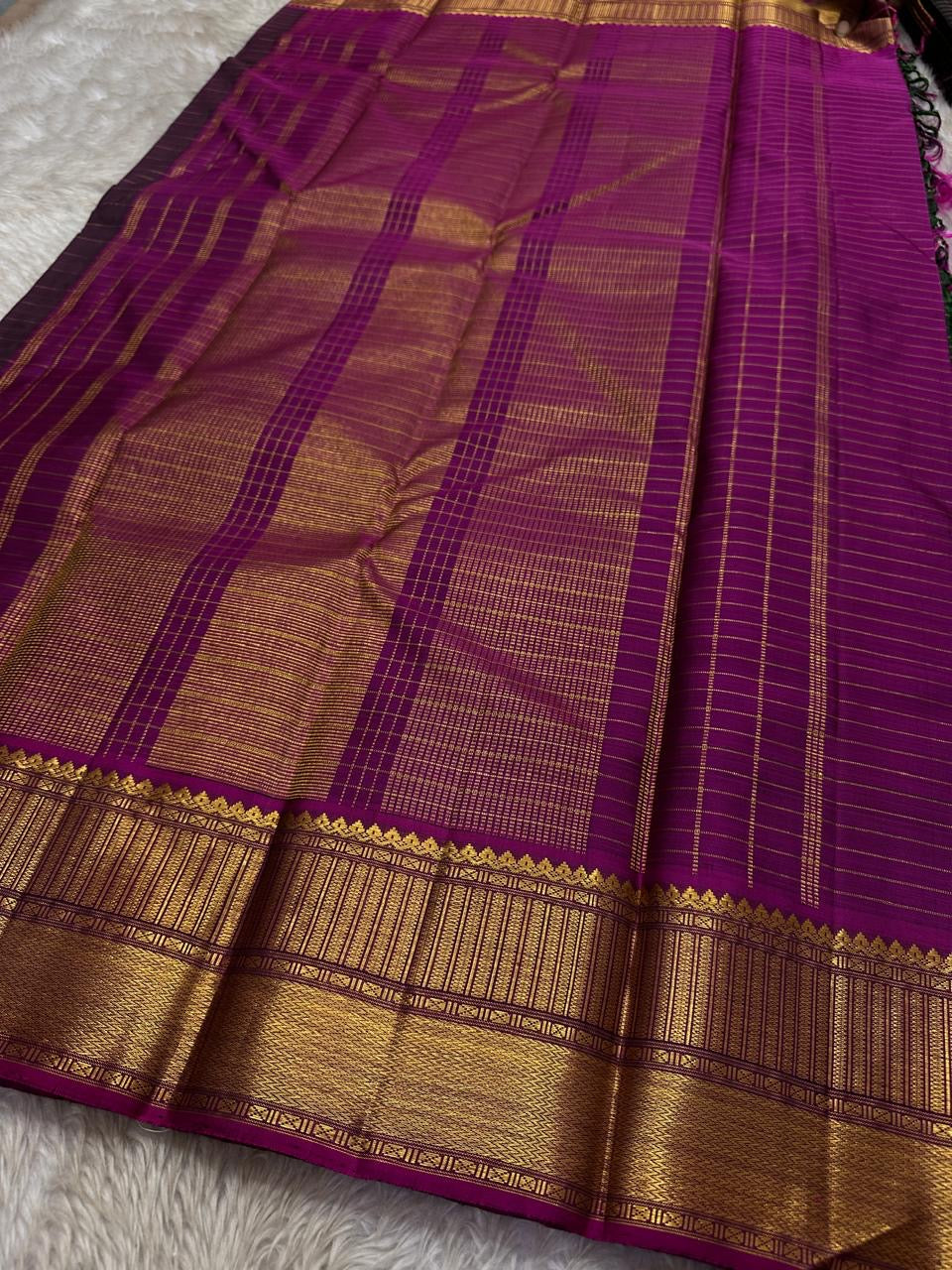 Pachai Zari Kattam – Pure Kanchipuram Silk Saree
Deep Emerald Green Body with Gold Zari Checks
Broad Golden Border with Magenta Highlights & Temple Motifs
Royal Magenta Pallu with Lustrous Zari Stripes
Silk Mark Certified, delivery in 2 weeks