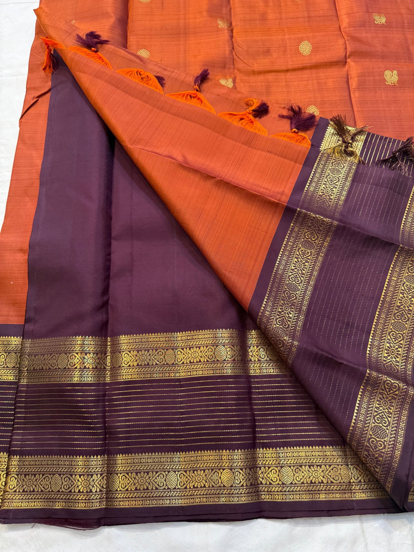 🧡 
Swarnamala — Korvai Kanchipuram Pure Silk
Rust-orange body with radiant gold chakram buttas
Deep purple korvai borders with rich zari detailing
Striped zari brocade pallu with temple-inspired motifs
Silk Mark Certified • Free Shipping within USA