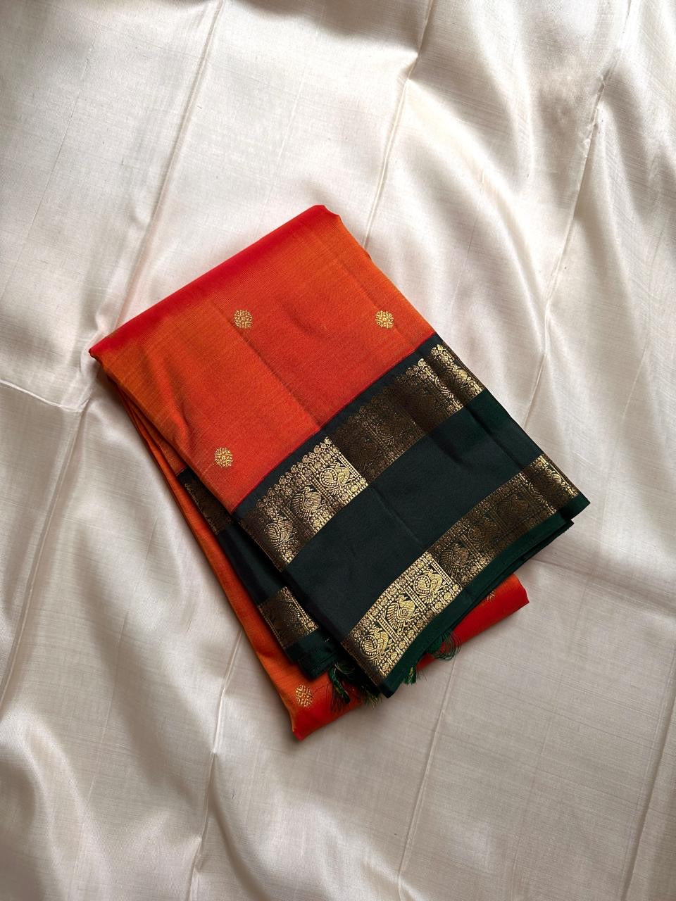 Riya – Orange Silk Saree with Dark Green Zari Border
Radiating warmth and festive charm, Riya glows in a rich ombré of orange and vermilion, adorned with dainty gold butta motifs that shimmer gently with movement.