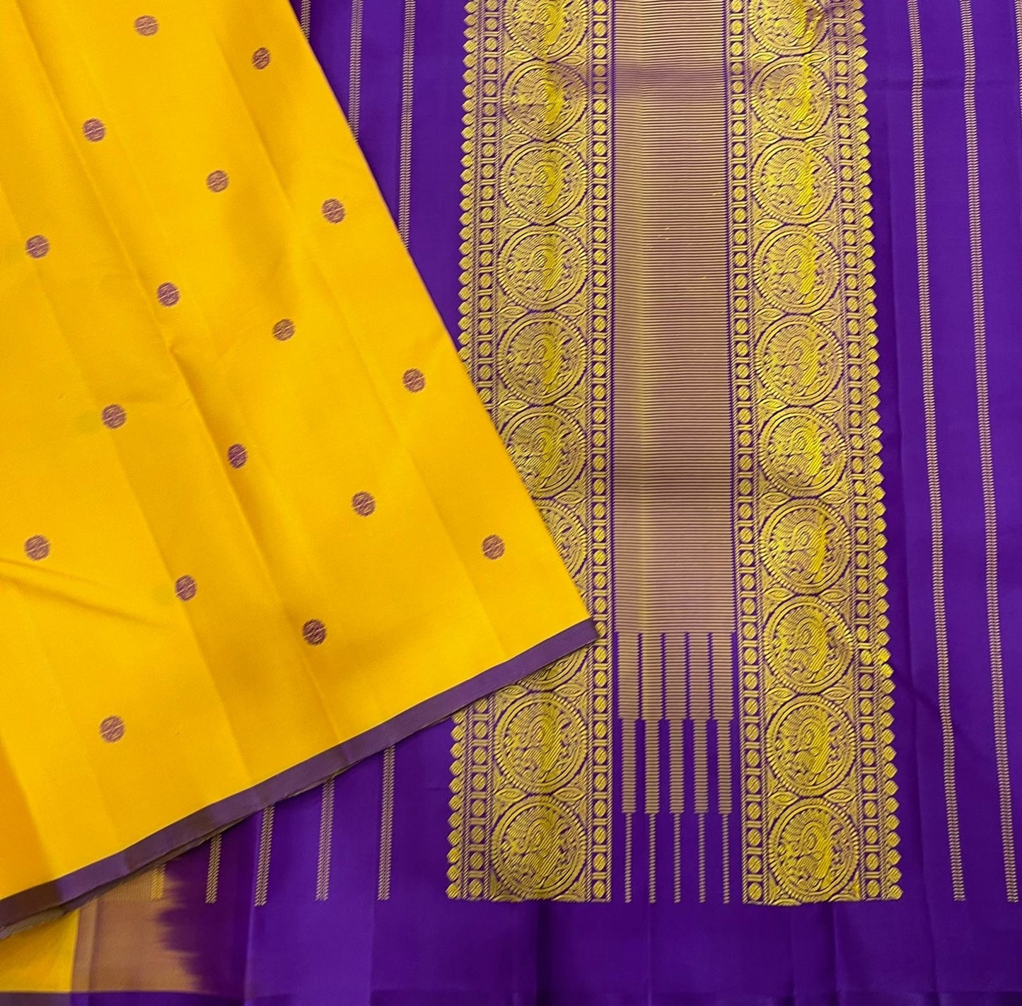 Manjal Vadamalli Chakram – Pure Kanchipuram Silk Saree
Marigold yellow body with purple floral thread buttas
Grand royal purple pallu with gold medallion zari & reku-style stripes
Handwoven Double Warp Weave | Silk Mark Certified | Fall & Pico Done