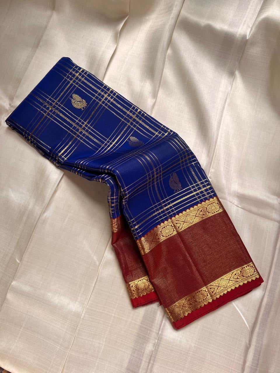 Sapphire Ruby Kattam – Pure Kanchipuram Silk Saree
sapphire blue body with gold kattam checks & buttas
Contrast ruby-red korvai borders with intricate gold zari weave
Grand ruby-red pallu with floral motifs
Silk Mark Certified | ships in 2 weeks