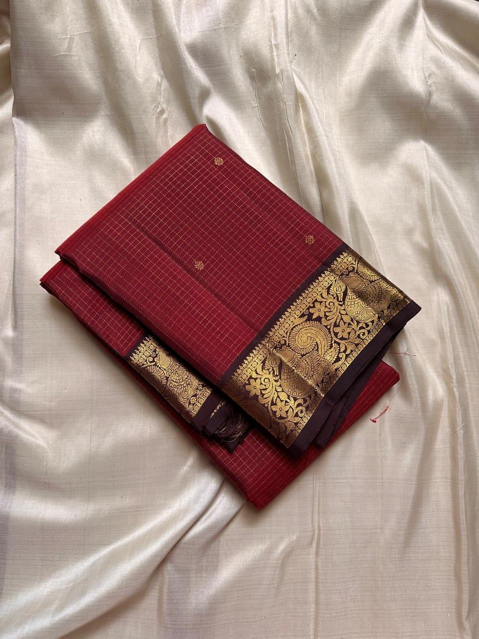 Mantra – Ruby Red coffee brown Kanchipuram Silk Saree with zari Checks with small buttas all over and Antique Peacock zari Border showcasing regal peacocks and floral vines. A richly detailed pallu completes this heritage Zari kattam