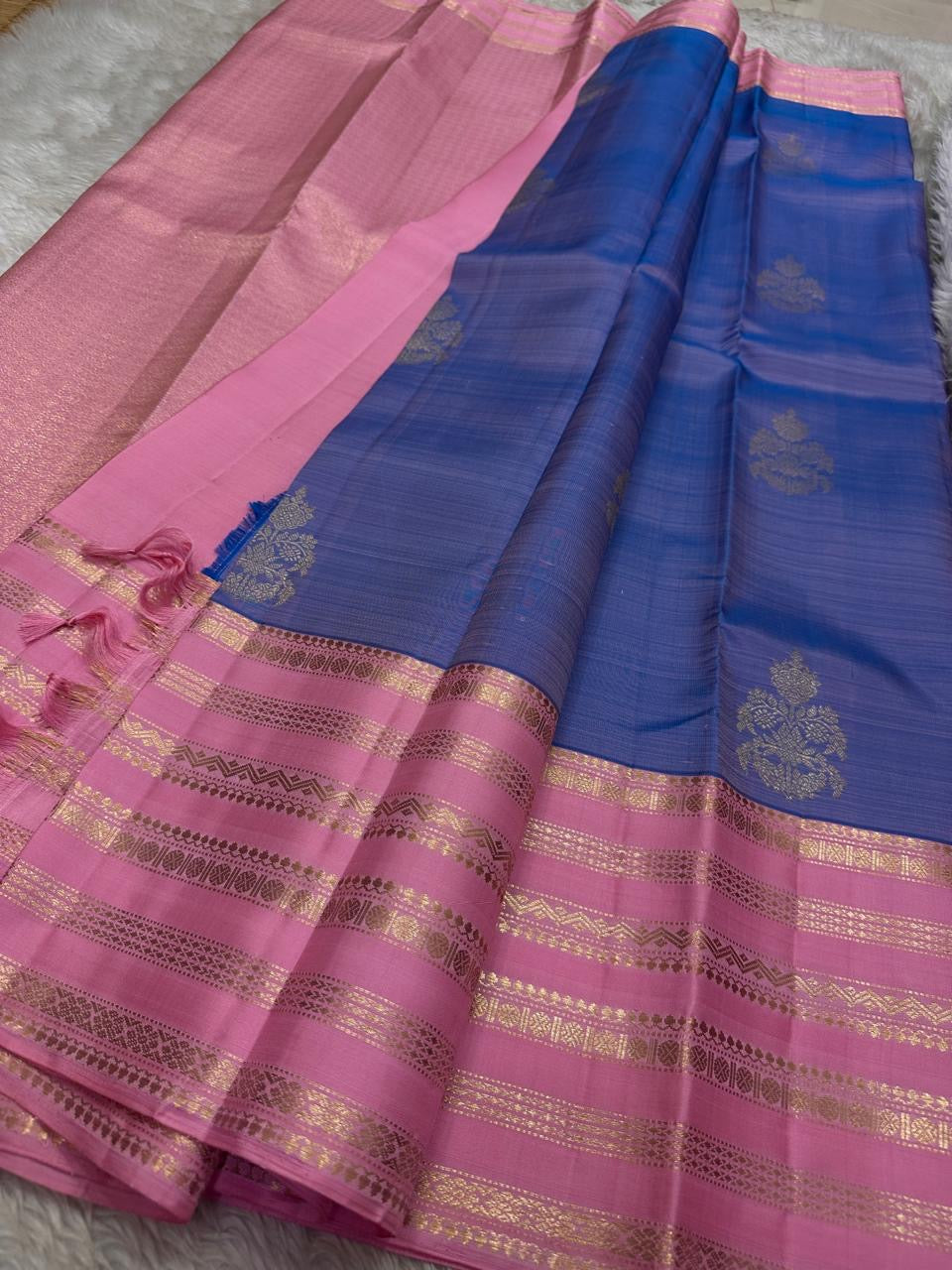 Ramyam, meaning pleasant and delightful, features a mesmerizing blue–purple shot body that shimmers with every movement. Its radiant pink korvai border and pallu, adorned with traditional Varisaipet zari stripes, add festive brilliance.silk mark certified
