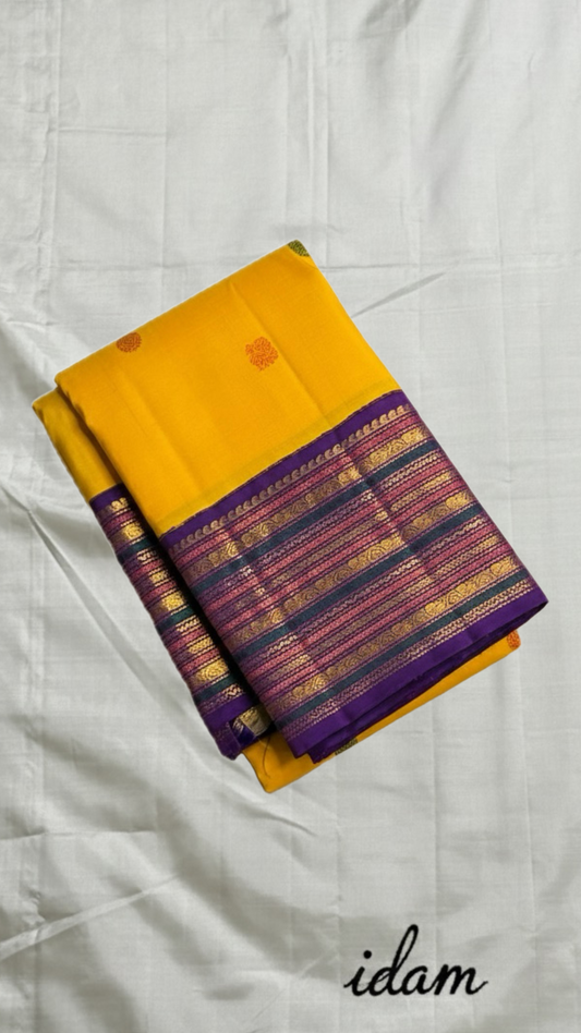 Swarna Kanakam Mayil Chakram — Pure Kanchipuram Silk Saree
Radiant turmeric-gold body adorned with silk-thread mayil and chakram buttas, framed by a regal vadamalli zari-woven korvai border and rich purple pallu.
Silk Mark Certified • Blouse Stitching Ava
