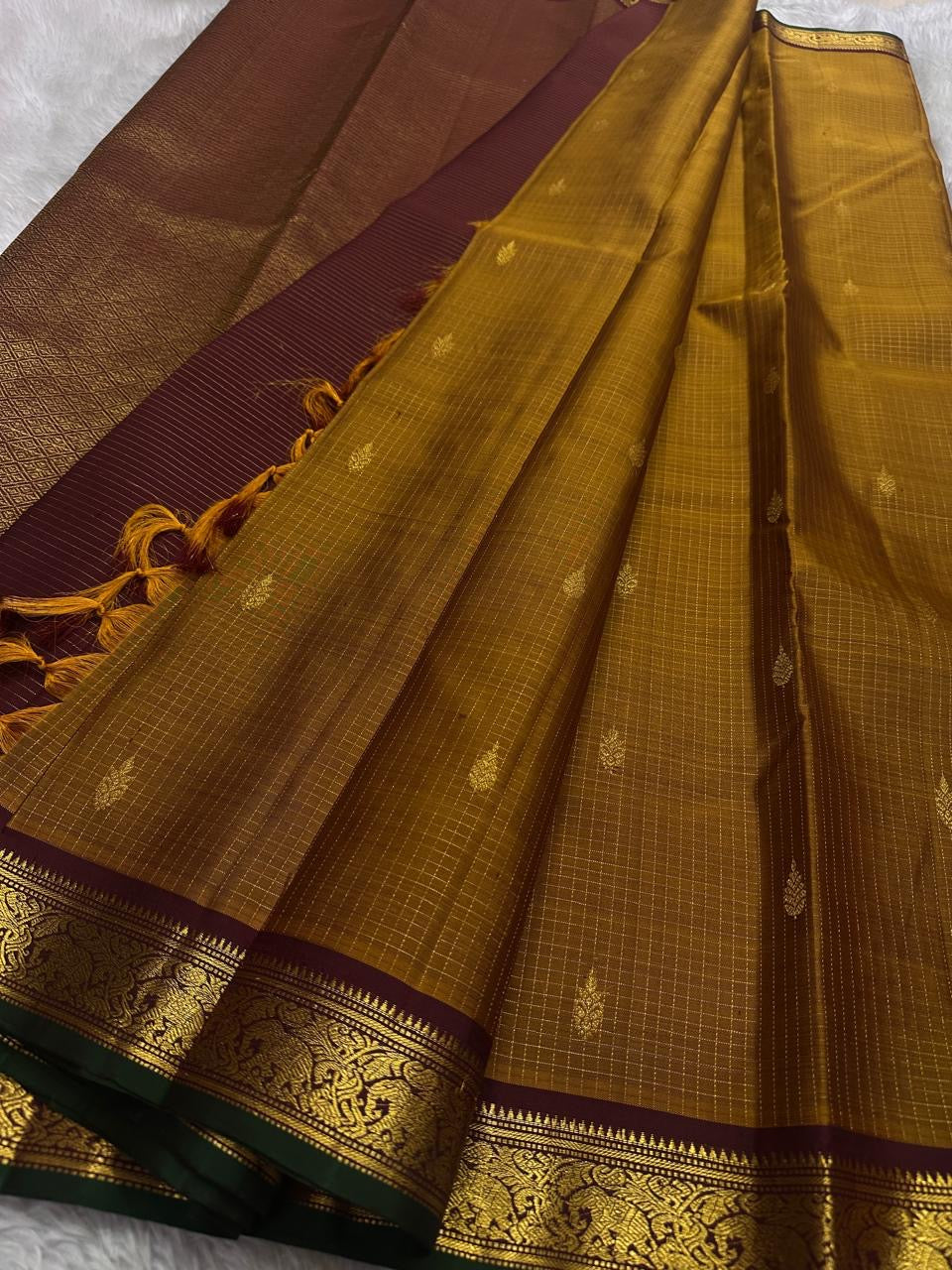 Amber Oosikattam ✨ – Pure Kanchipuram Silk Saree
Burnished Amber-Gold Body in Oosi Zari Kattam with Leaf Buttas
Deep Maroon Korvai Border with Green Selvedge & Elephant Motifs
Regal Maroon Pallu with Intricate Gold Zari Brocade
Silk Mark Certified |