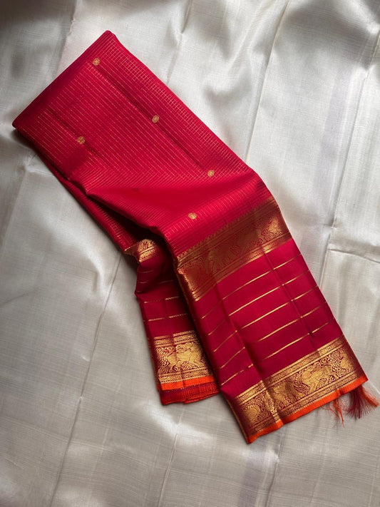 Partly opened pink-red Kanchipuram silk saree showing fine pinstripes, small gold buttas and gold lined border.