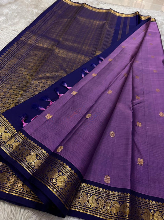 Lilac Mayil Pushpam – lilac-purple body with navy korvai borders
Pure Kanchipuram silk • gold zari pushpam (flower) buttas all over
Grand navy brocade pallu with diamond jaal • contrast blouse with border
Silk Mark Certified | Fall & Pico Done |