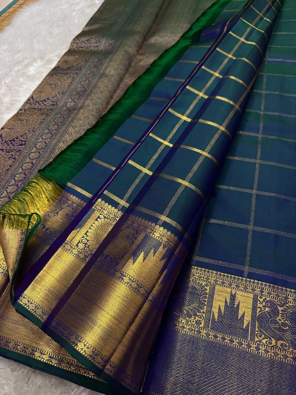 A celestial blend of blue and green, this Kanjivaram silk saree ,adorned with Gandaberunda and Kamalam buttas, golden checks, and a majestic thazhampoo Mayil border. Zari kattam