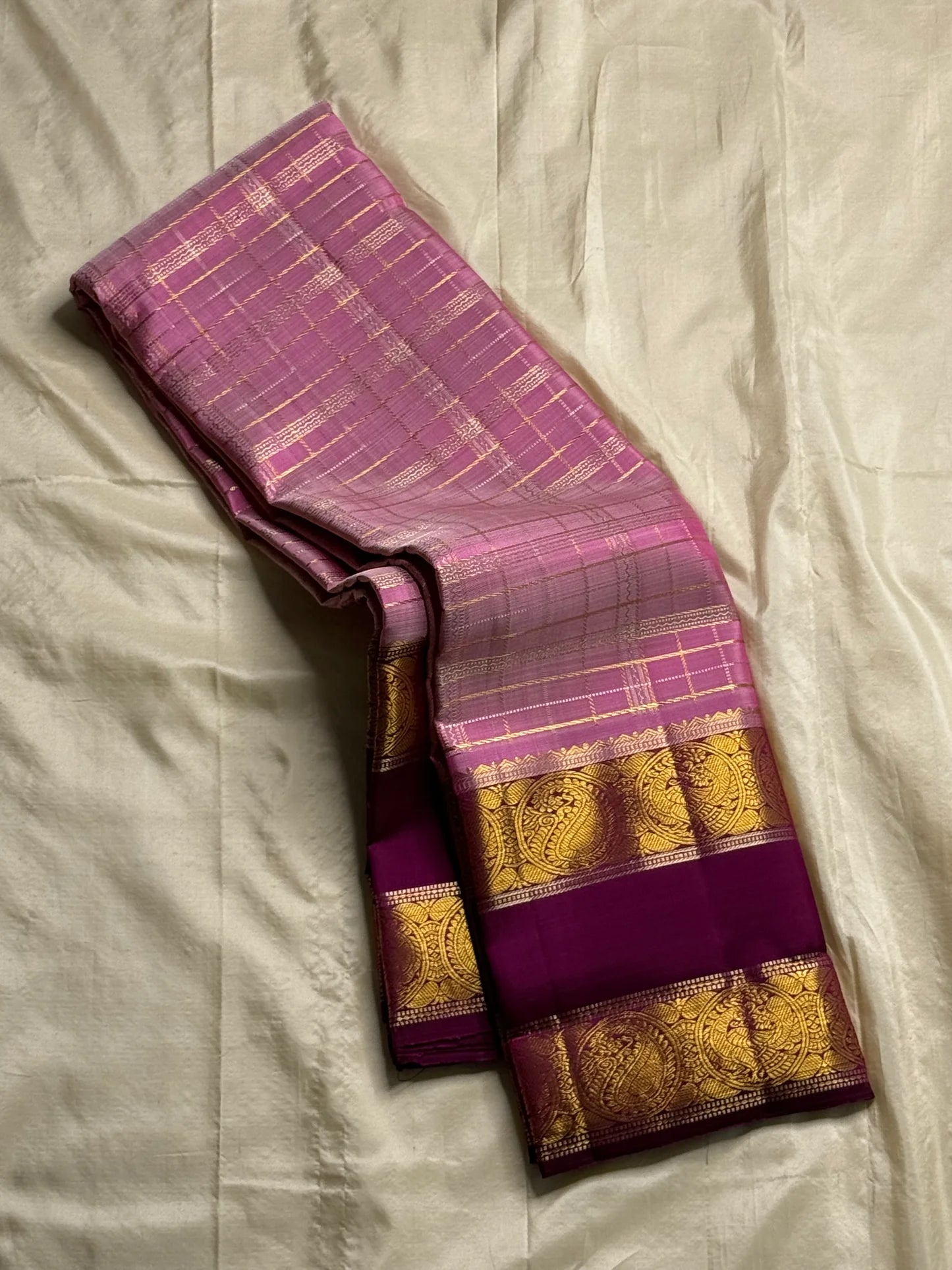 Mauve Mayil Mukham — Kanchipuram Pure Silk
Pastel-mauve pink  body with delicate zari wide kattam checks
Deep plum korvai border with grand mayil (peacock) chakram motifs
Copper-rose chevron zari pallu & plum contrast blouse
Silk Mark Certified • Free