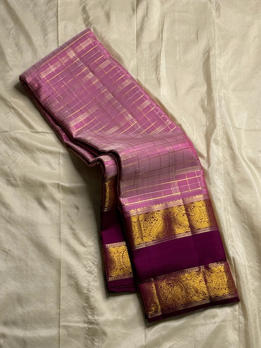 Mauve Mayil Mukham — Kanchipuram Pure Silk
Pastel-mauve pink  body with delicate zari wide kattam checks
Deep plum korvai border with grand mayil (peacock) chakram motifs
Copper-rose chevron zari pallu & plum contrast blouse
Silk Mark Certified • Free