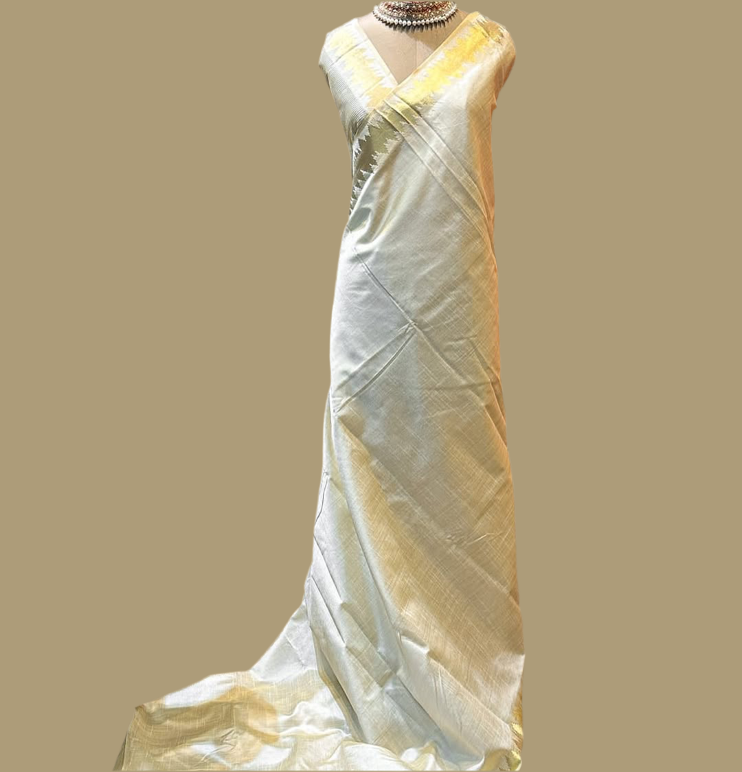 Minimal yet majestic, this ivory-beige silk saree is a celebration of simplicity and sophistication. The body is plain and luminous, texture of the silk shines through. golden zari border with a sharp, zigzag temple-inspired pattern - perfect for Onam