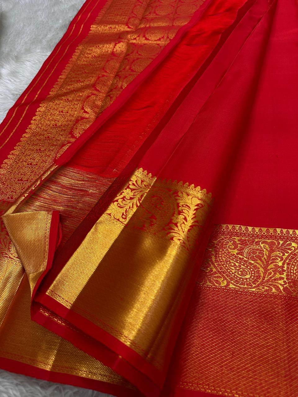A traditional Kanjivaram (Kanchipuram) silk saree, vibrant red orange peacock floral motifs bavanji border and ornate grid motif Pallu