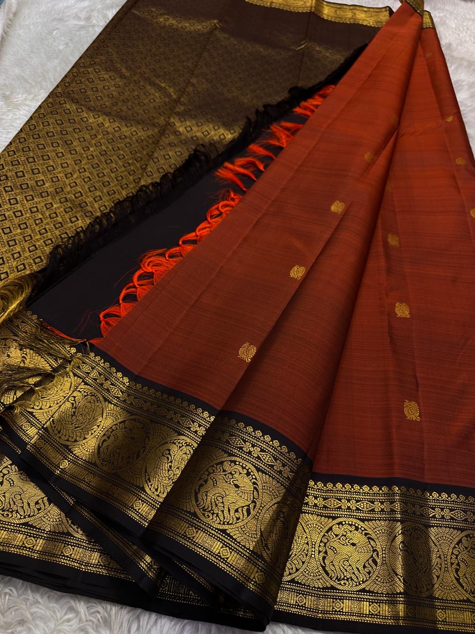 Rust Orange Prabhavali – Pure Silk Kanchipuram
Rust-orange body with golden zari buttas ✨
Deep black korvai borders with grand Annam medallions 🪔
Opulent black brocade pallu with diamond jaal & tassels 🌿
Silk Mark Certified • Ships in Two Weeks • Free S