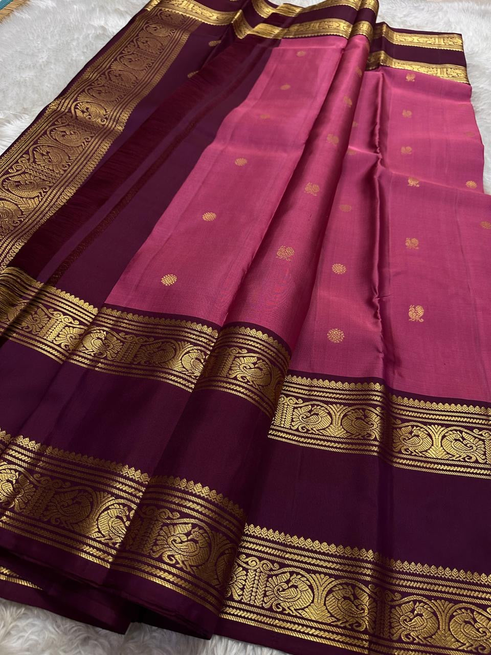 Saanvi – Lotus Pink & Magenta Shot Kanchipuram Silk Saree
Saanvi features zari buttas of mayils and chakrams across the body. A deep wine rettapettu border showcases twin peacocks in a temple arch. The pallu mirrors this grandeur with sorgavasal motifs !
