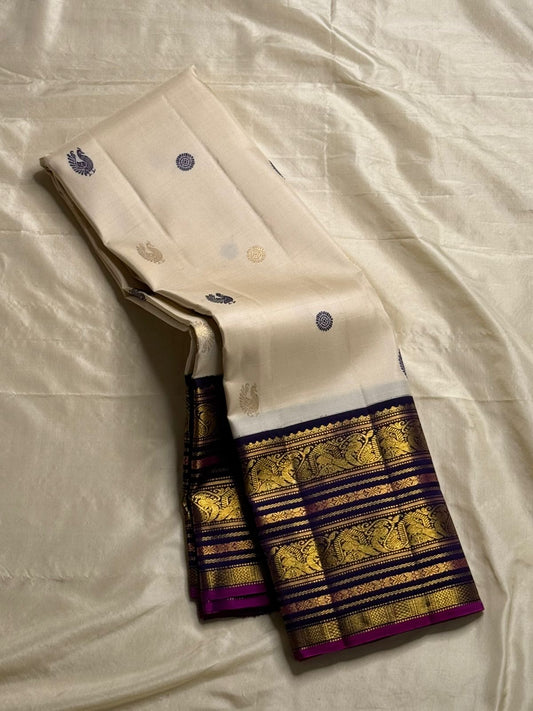 Ivory Vadamalli Annam Chakram – Korvai Kanchipuram Silk Saree
Ivory body with navy & gold chakram and peacock buttas
Vadamalli korvai border with annam panels & vine zari
Rich zari-brocade pallu | Contrast vadamalli blouse 
Silk Mark Cert. Ships in 2 week