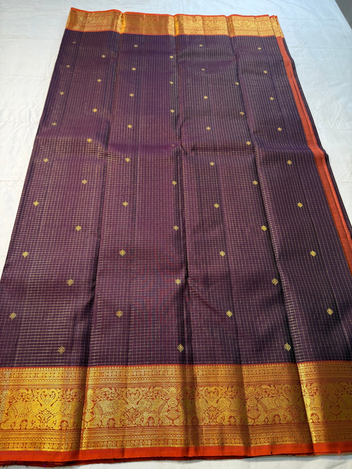 Deep Plum Orange
A regal dance of plum and burnt orange
Micro-checks kissed with golden buttas
Elephant borders marching in heritage grandeur
Brocade pallu glowing in timeless zari brilliance
Silk Mark Certified, delivery in 2 weeks