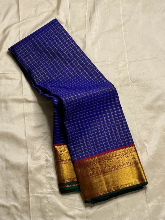 Neela Ratnam — Pure Silk Kanchipuram
• Cobalt-blue kattam checks with antique-gold zari
• Ruby-maroon contrast pallu with grand zari work
• Floral vine borders with bottle-green selvedge
• Silk Mark Certified • Ships in Two Weeks • Free Shipping withi