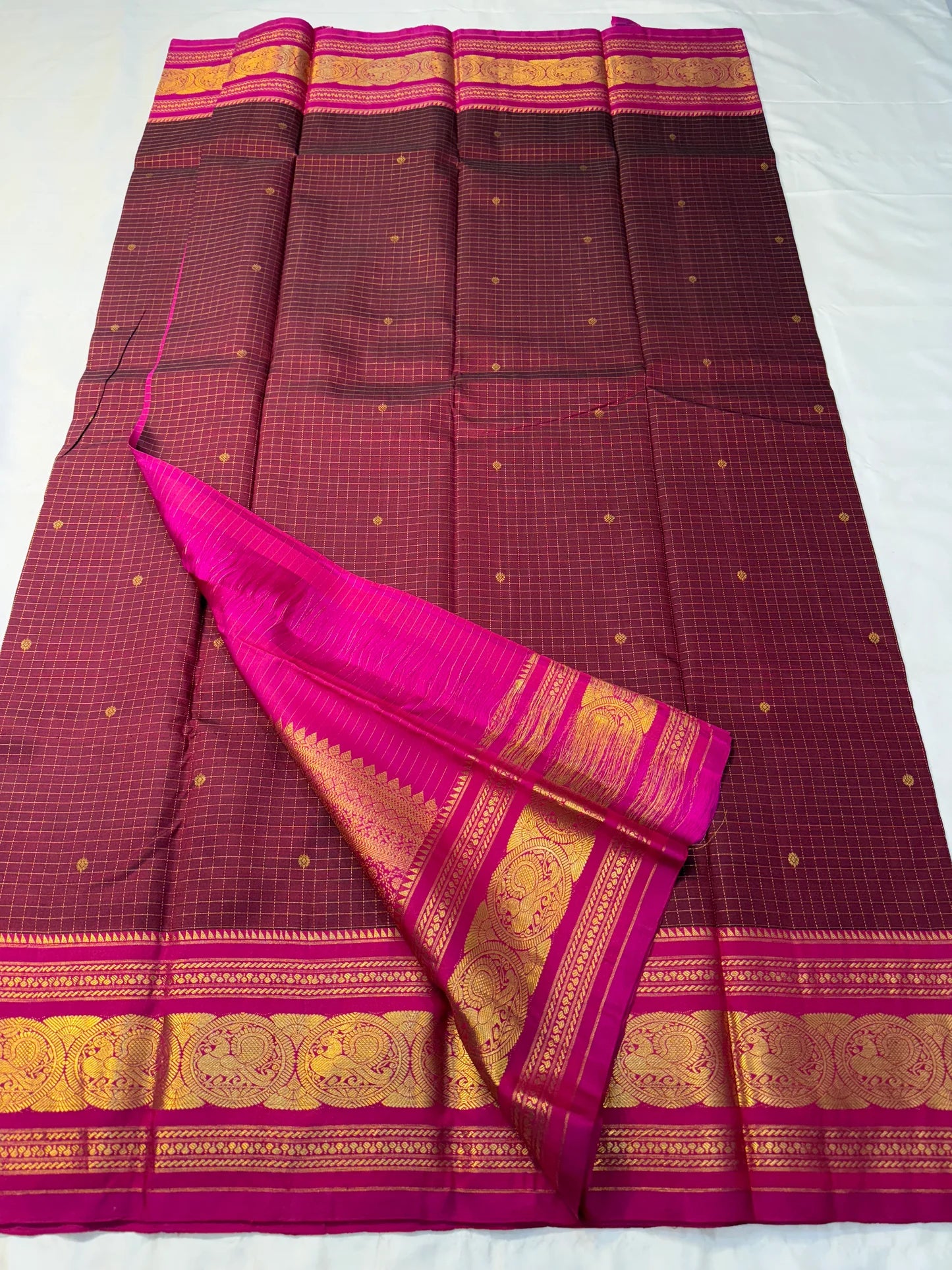 Arakku Kattam Mayura Chakram – Pure Silk Kanchipuram Saree (Maroon & Rani Pink)
Micro-check body with tiny gold buttas; vibrant rani contrast
Antique-gold peacock chakram border & grand woven zari pallu
Silk Mark Certified | Blouse Piece Included |