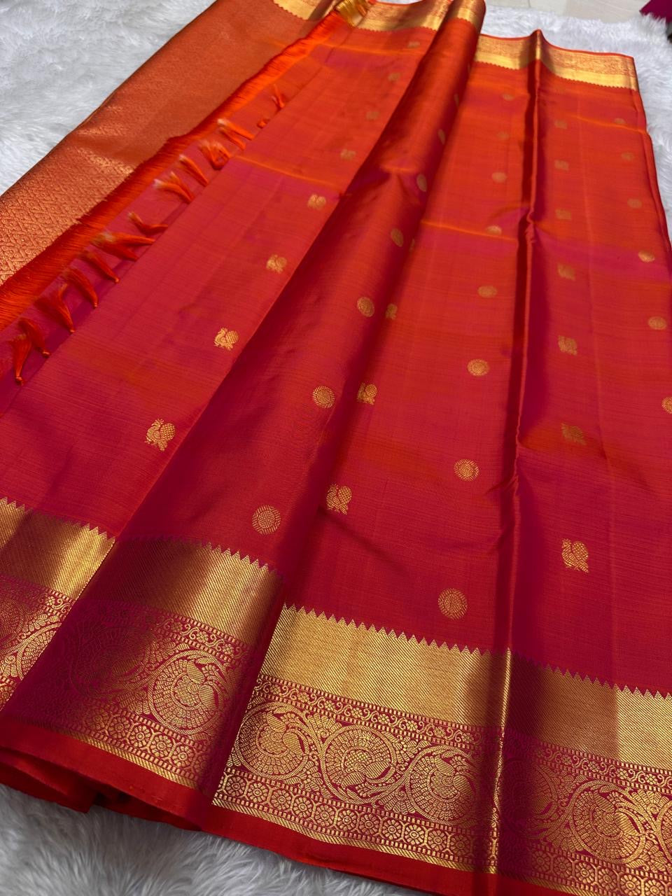 Agnika – Tomato orange shot Red Kanchipuram Silk Saree with Mayil Chakram Butta & Orange Border
Fiery and regal, Agnika is a pure Kanchipuram silk saree featuring a rich red body adorned with intricate Mayil Chakram buttas.