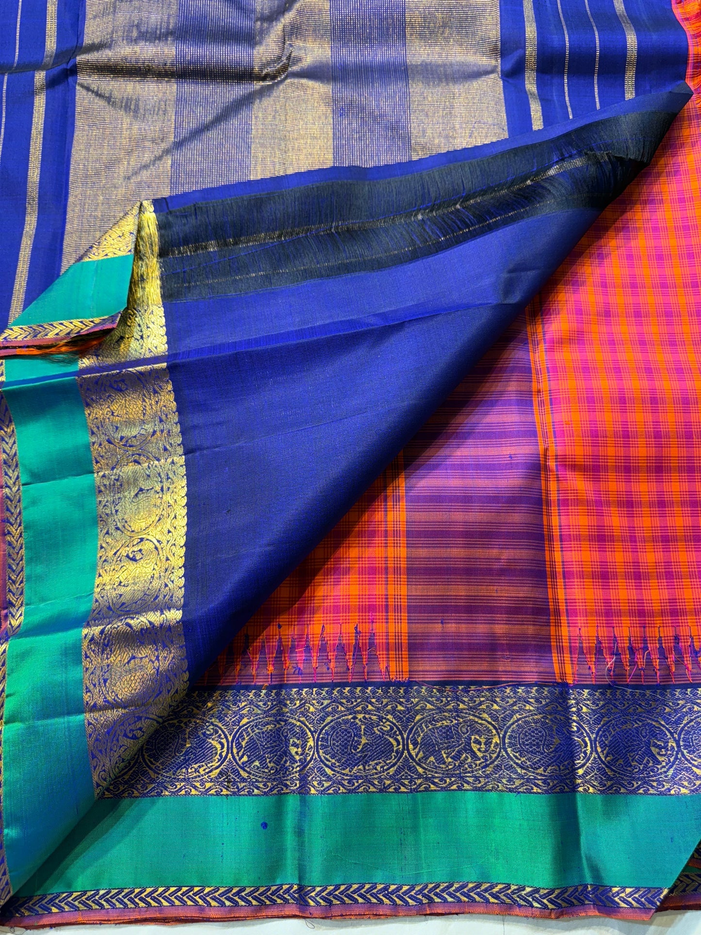 Chemman Maragatha Kattam
Pure Kanchipuram Silk Saree – Reddish-Orange & Maragatha Green Micro Checks
Deep violet korvai borders with gold zari floral motifs
Grand zari pallu with classic brocade detailing
Silk mark certified, ships in 2 weeks