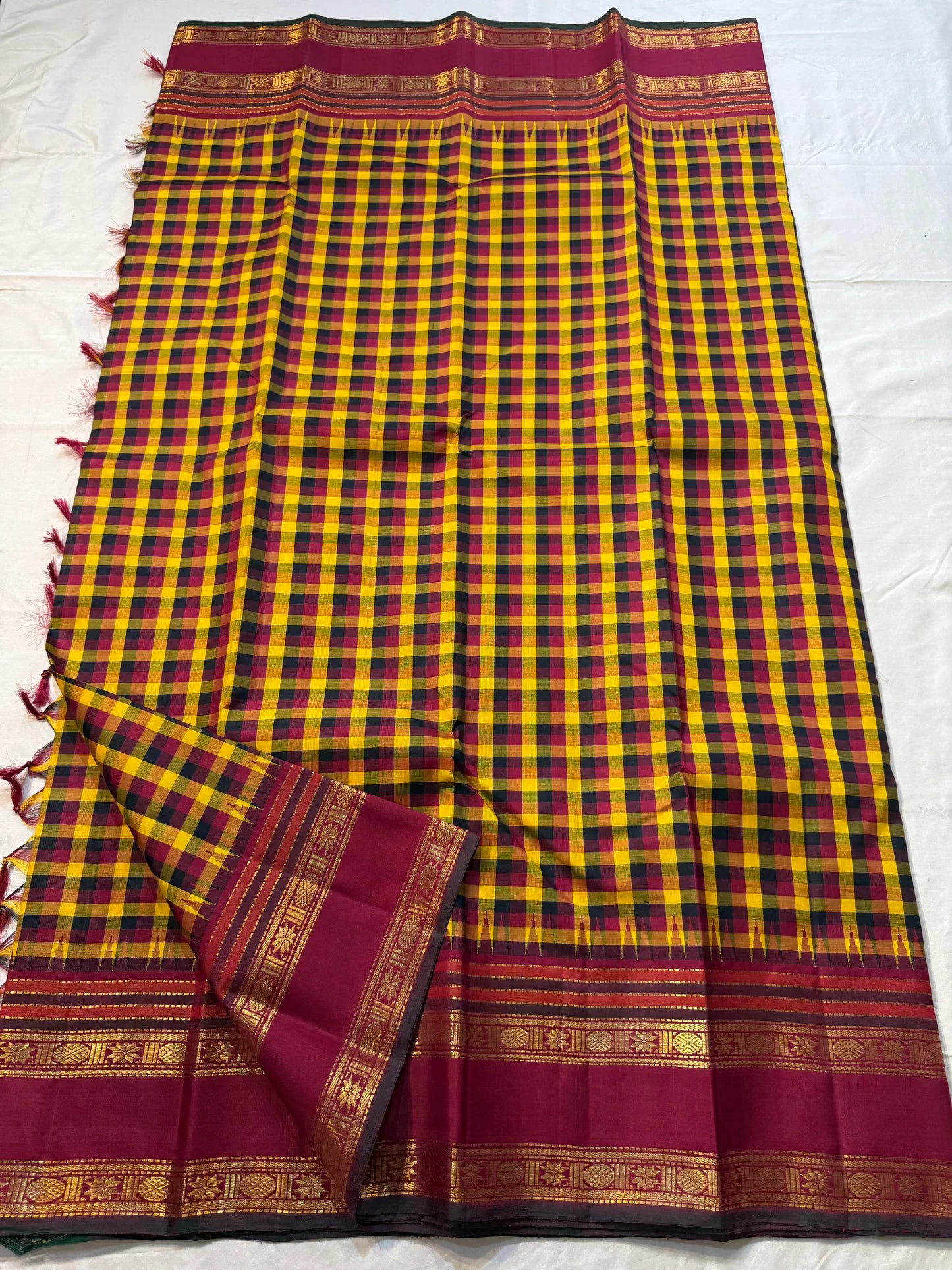 Manjal Maroon Kattam – Pure Kanchipuram Silk Saree
Mustard & Maroon Body with Traditional Multi-Color Checks
Korvai Borders with Floral-Star Zari & Temple Tips
Grand Maroon Pallu with Gold Zari Stripes & Tassels
Silk Mark Certified | ships in 2 weeks