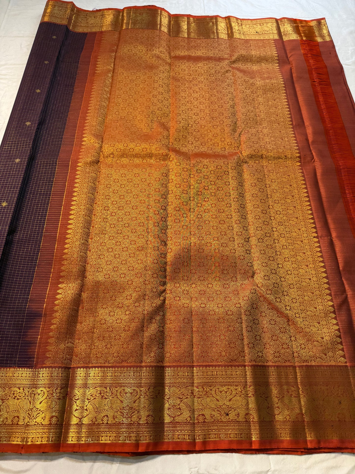 Deep Plum Orange
A regal dance of plum and burnt orange
Micro-checks kissed with golden buttas
Elephant borders marching in heritage grandeur
Brocade pallu glowing in timeless zari brilliance
Silk Mark Certified, delivery in 2 weeks