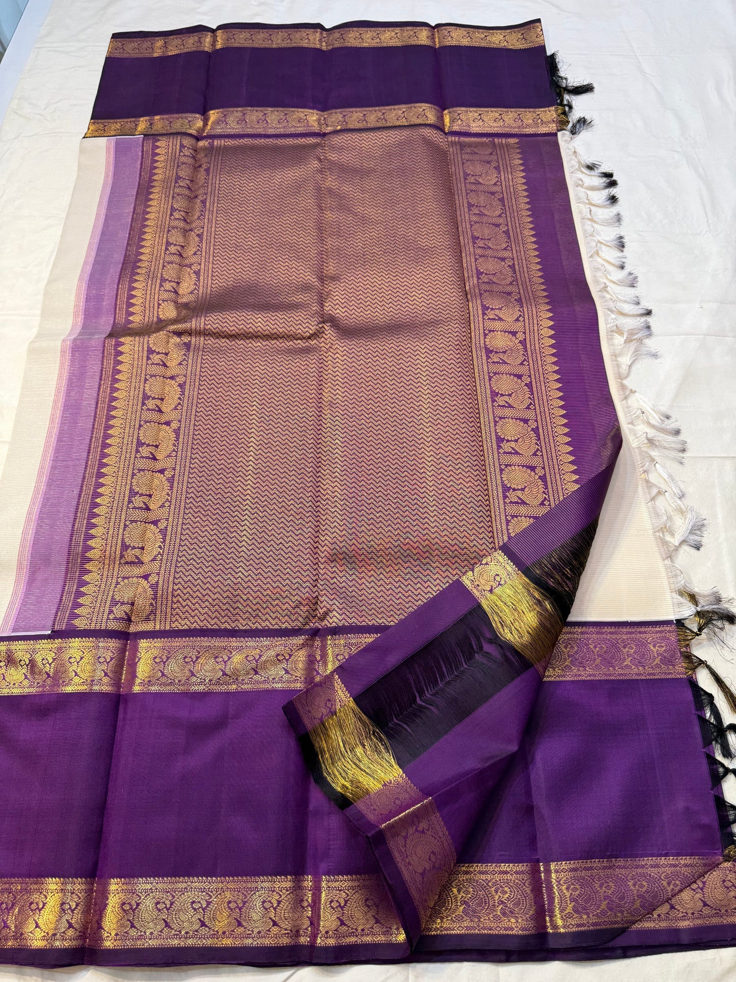 Ivory Violet Vairaoosi — Pure Silk Kanchipuram Saree
Pearl-Ivory Vairaoosi Body with Gold Round Buttas ✨
Deep Violet Korvai Border & Chevron Zari Pallu • Silk Mark Certified • Free USA Shipping • ships in 2 weeks
