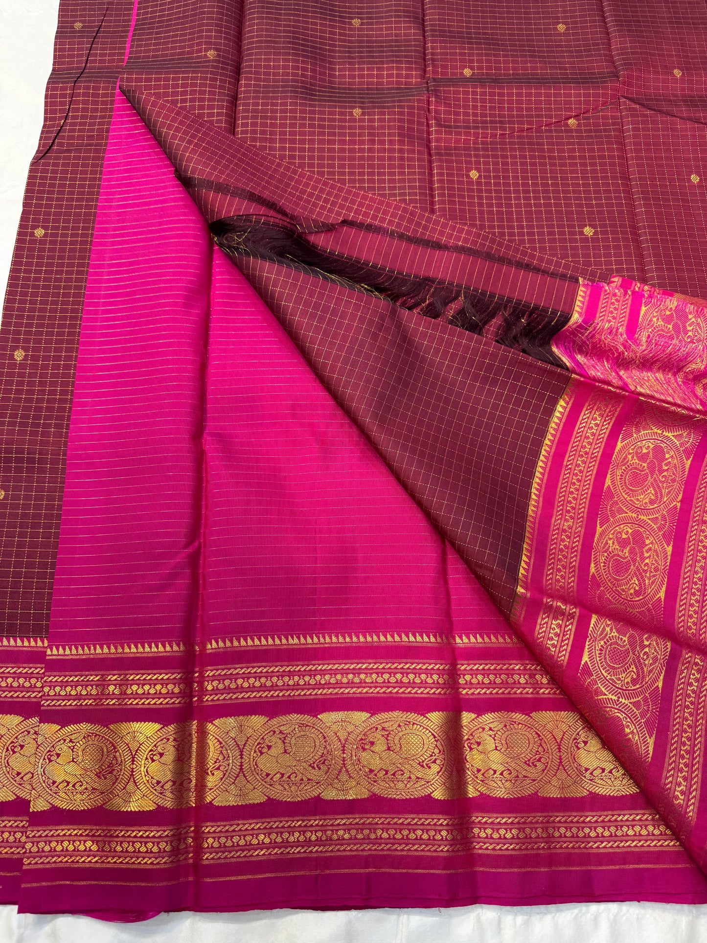 Arakku Kattam Mayura Chakram – Pure Silk Kanchipuram Saree (Maroon & Rani Pink)
Micro-check body with tiny gold buttas; vibrant rani contrast
Antique-gold peacock chakram border & grand woven zari pallu
Silk Mark Certified | Blouse Piece Included |