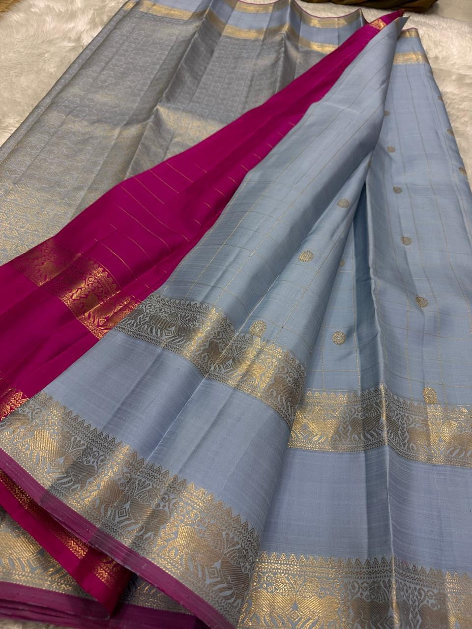 Fuchsia in Sky – Pure Silk Kanchipuram Saree
Sky Blue Body with Gold Kattam Checks & Petite Buttas
Fuchsia Contrast Petni Pallu with Zari Reku Stripes
Wide Gold Zari Border with Peacock & Temple Motifs
Silk mark certified, ships in 2 weeks