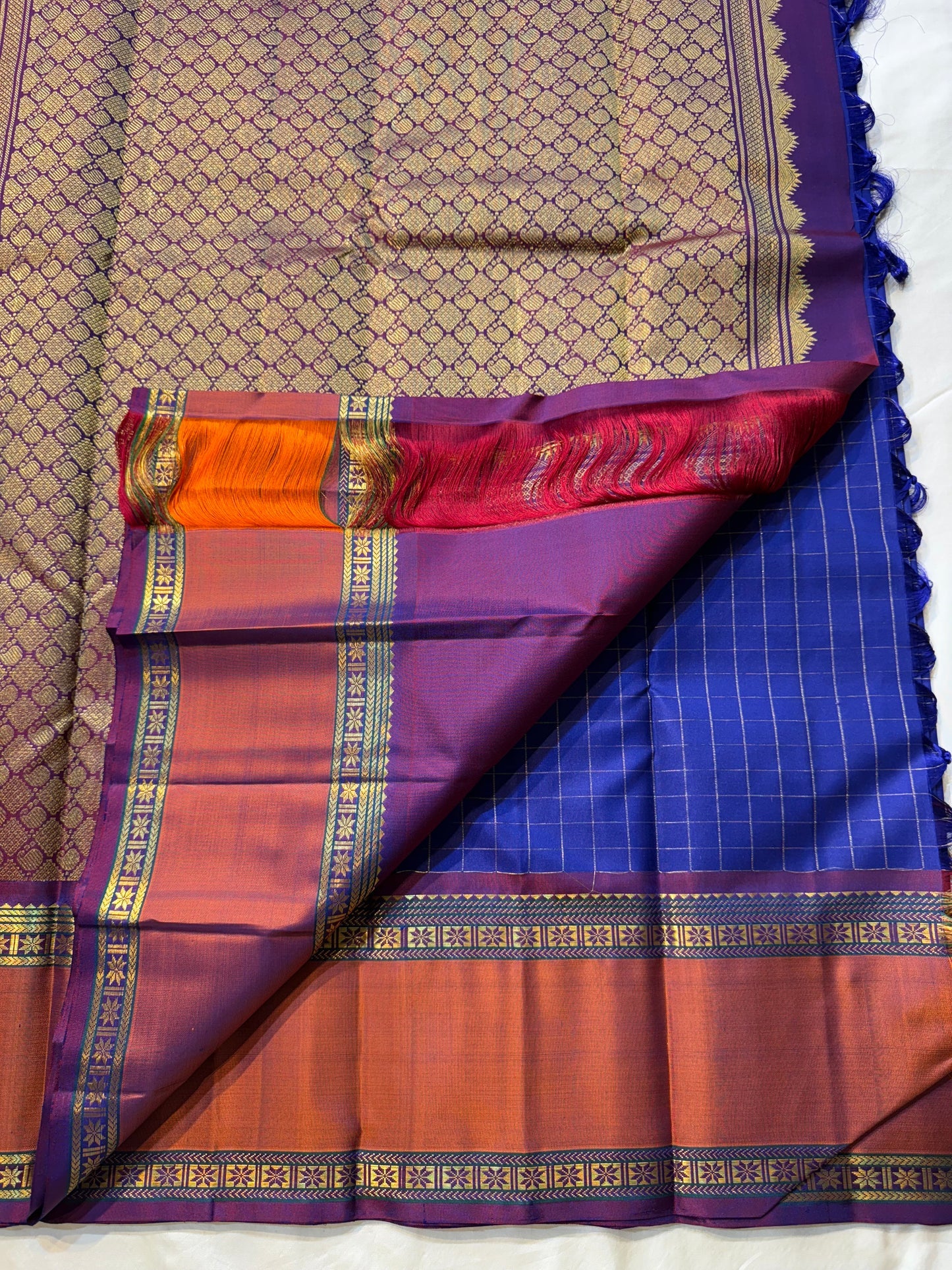 Indra Neelam Kattam – Pure Kanchipuram Silk Saree
Royal Blue Body with Fine Zari Grid Checks
Copper-Rose Korvai Borders with Floral & Chevron Zari
Grand Purple Pallu with Tassels
Silk Mark Certified | ships in 2 weeks | Blouse Stitching Available