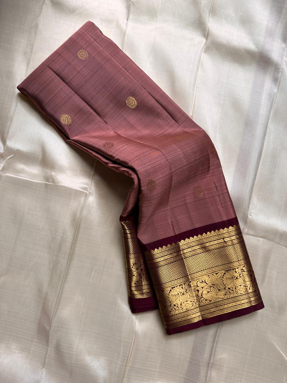 Mauve Buttas – Pure Kanchipuram Silk Saree
Ethereal mauve body adorned with buttas ✨
Borders rich in regal zari with floral and animal artistry 🌿🦚
Grand pallu woven in opulent gold jaal, exuding heritage charm 💫 Silk Mark Certified, delivery in 2 weeks