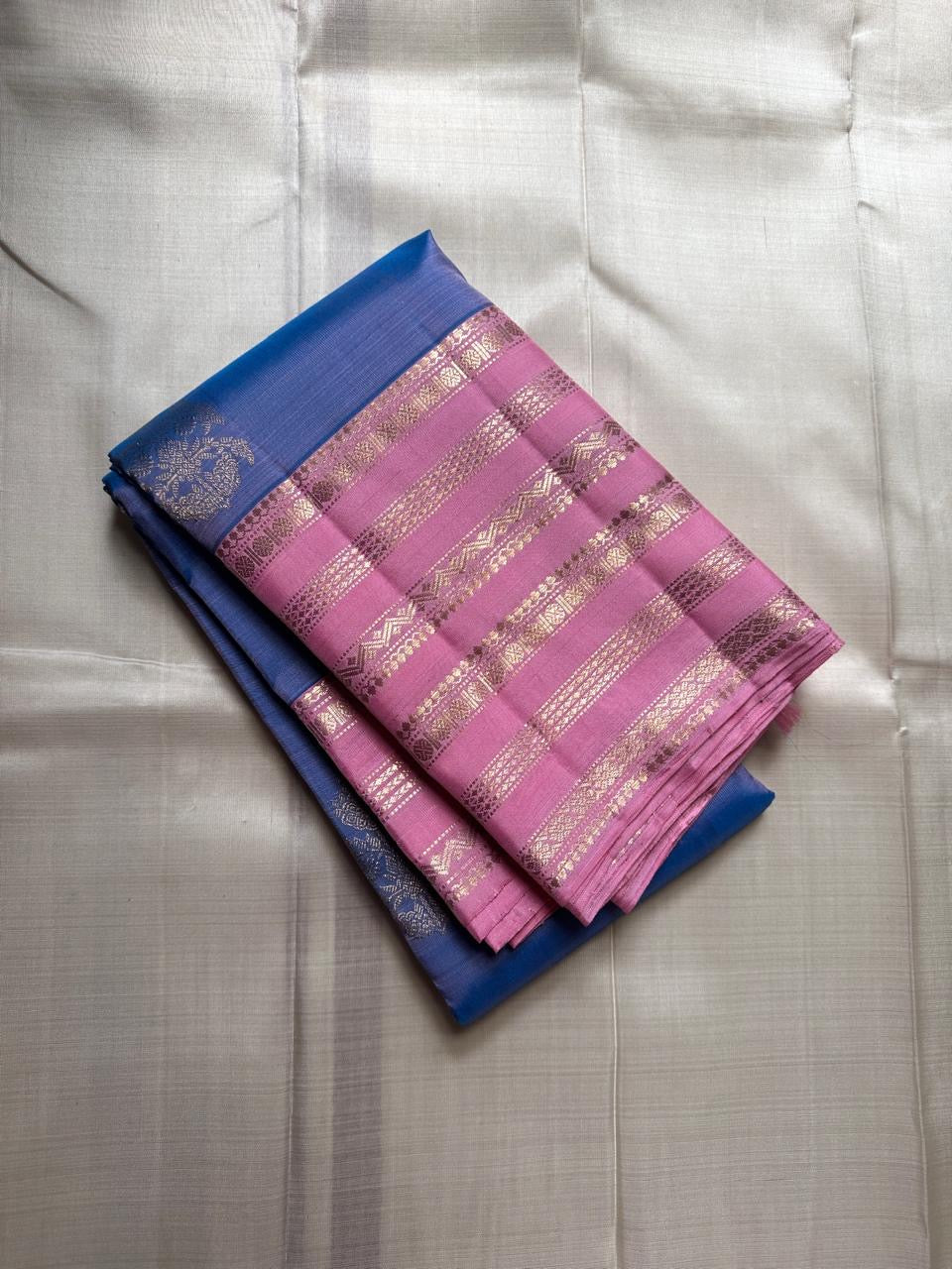 Ramyam, meaning pleasant and delightful, features a mesmerizing blue–purple shot body that shimmers with every movement. Its radiant pink korvai border and pallu, adorned with traditional Varisaipet zari stripes, add festive brilliance.silk mark certified