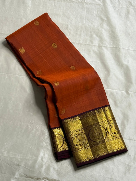 Rust Orange Supreme – Korvai Kanchipuram Pure Silk Saree
Shot rust-orange body with gold chakram & mankolam buttas all over
Deep purple korvai border with annam & chakram zari medallions
Rich vadamalli zari-brocade pallu | Contrast blouse | Fall & Pico Do