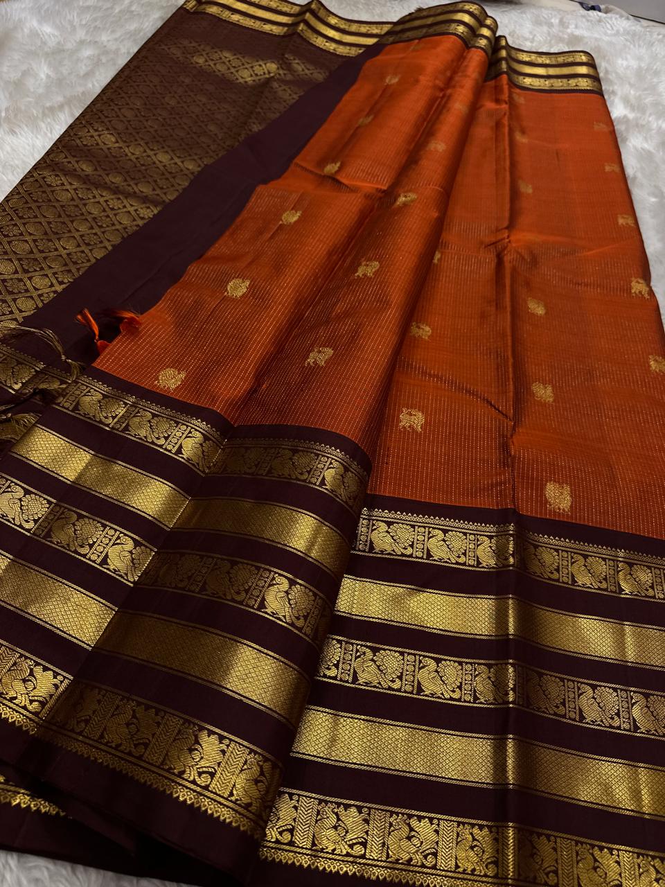 Ember Yazhi – Pure Kanchipuram Silk Saree
Burnt Orange Body with Vaira Oosi Stripes & Yazhi Buttas
Contrast Maroon Varisaipet Border with Gold Zari Panels
Grand Maroon Brocade Pallu with Intricate Motifs
Silk Mark Certified, delivery in 2 weeks