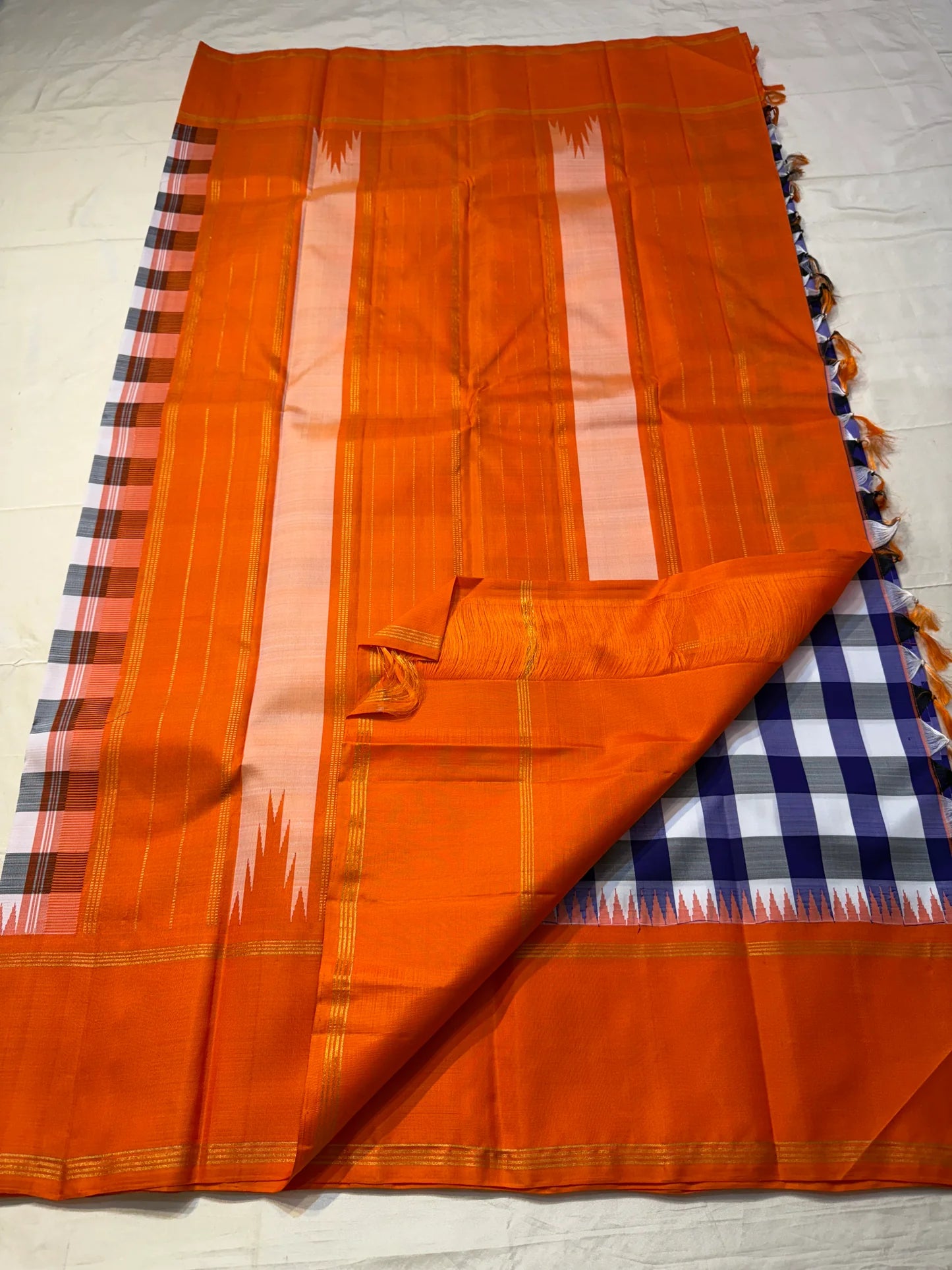 Indigo–Tangerine Checkmate — Pure Silk Kanchipuram
Bold indigo–lilac–white buffalo checks with ash accents ✨
Vibrant tangerine korvai border with temple (reku) teeth 🌸
Solid tangerine pallu with fine thread stripes & tassels 🪔
Silk Mark Certified •