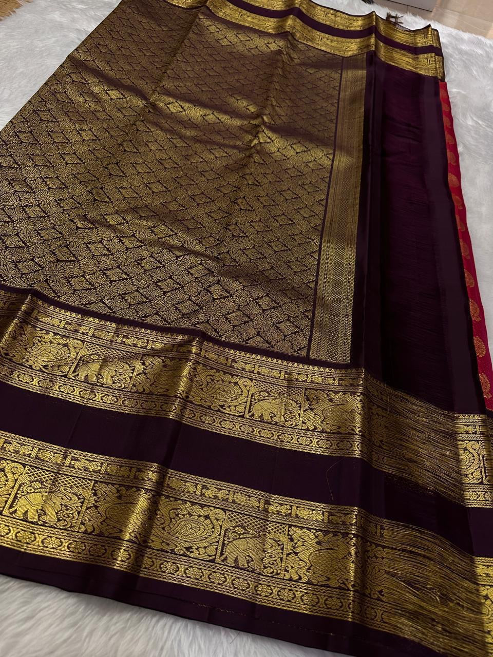 A regal shot tomato red pink Kanchipuram silk saree features elegant chakram and mayil gold zari buttas woven across the body. Brown contrast rettapet border and Pallu vanasringaram details