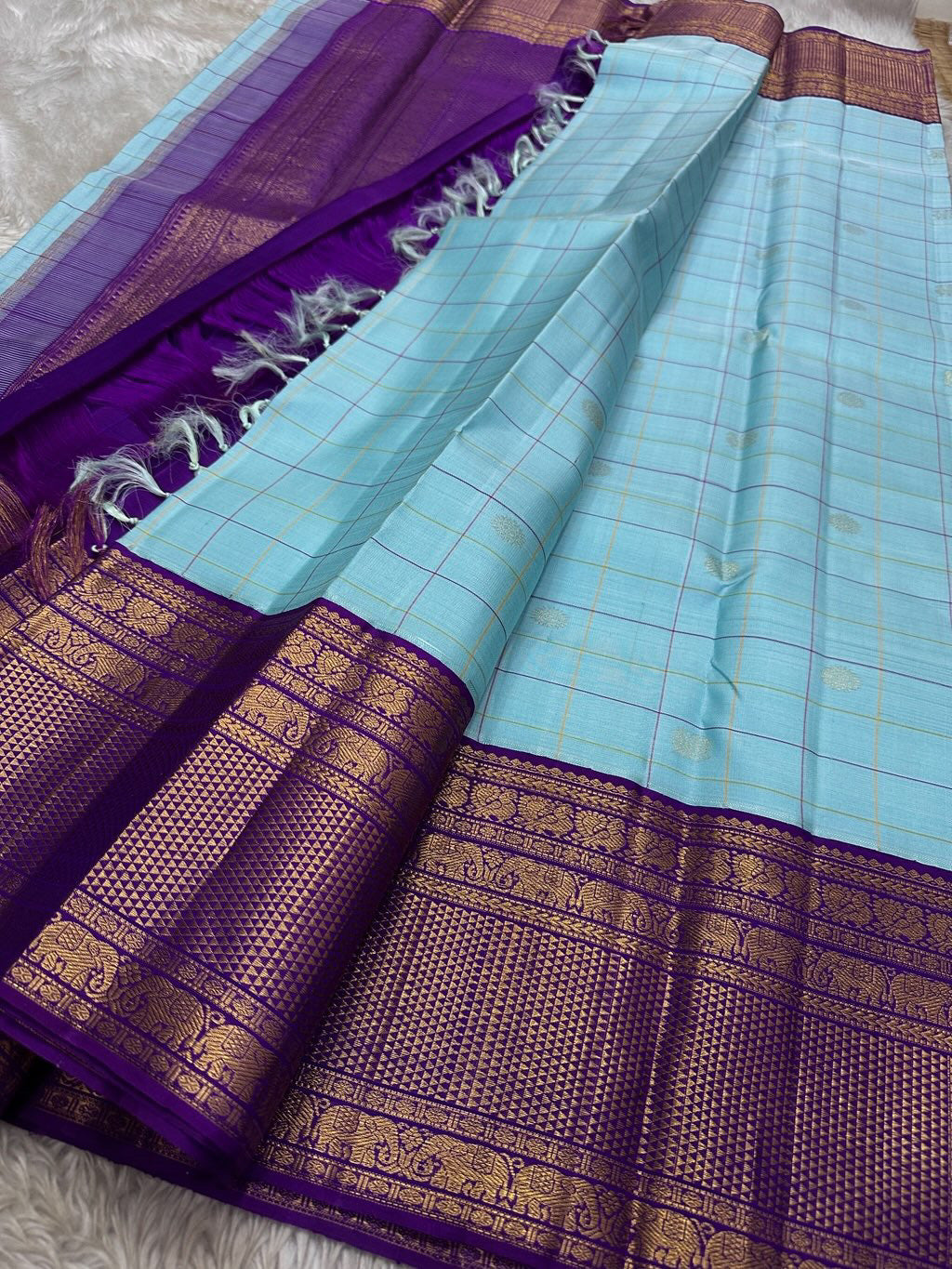 Aqua Amethyst zari kattam Pure Kanchipuram Silk Saree with blue Checks & Purple Border
Radiant sky-blue silk woven with delicate golden checks.
Grand purple korvai borders with elephant and floral motifs.
Silk Mark Certified, delivery in 2 weeks