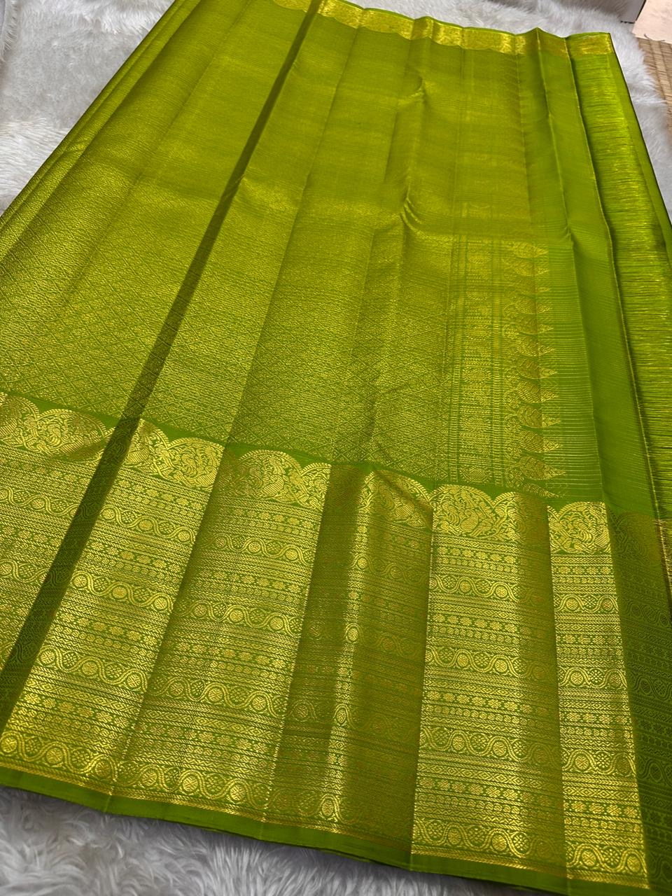 A radiant parrot green Kanchipuram silk saree that dazzles. The body features a delicate grid-like zari weave with small gold buttas scattered. The rich gold zari pallu stands out with grand temple-inspired arches and intricate motifs.