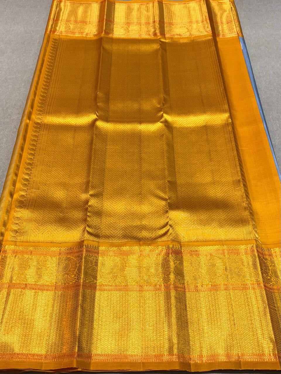 Eesha – Grey-Blue & Mustard Kanchipuram Pure Silk Saree.
Zari Butta All Over with Hamsa / Annapakshi Motifs in Arai Maadam border .
Detailed Chevron in pure 3g Zari Pallu with Muthu Seer Border for a Timeless Drape