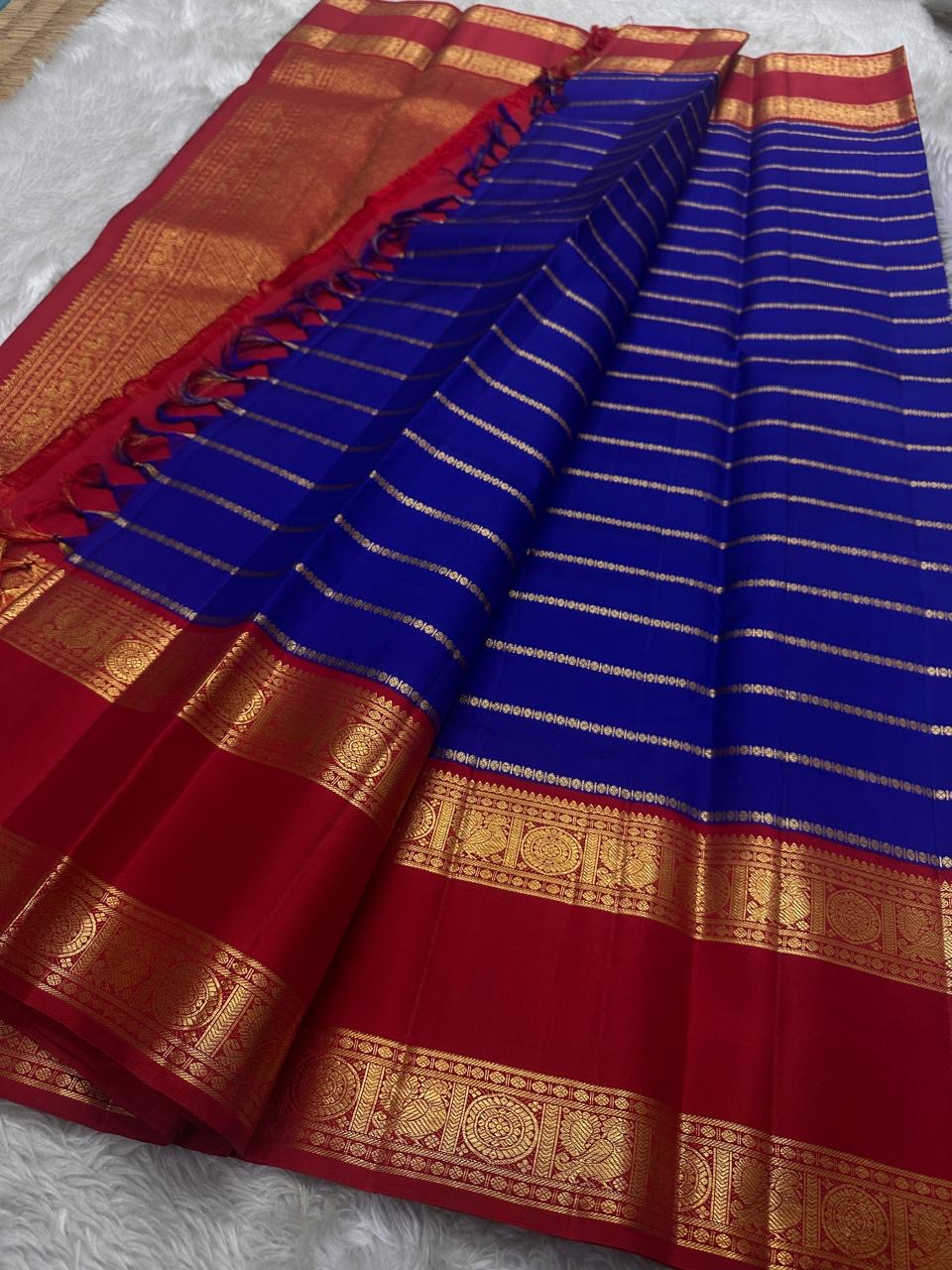 Meera – A Living Raga in Kanchipuram Silk: Draped in Crimson and Iconic MS Blue, Adorned with Gold Zari Seer, Muthu Borders, and Peacocks and kamalam , Woven in the Spirit of Classical Grace and Devotion