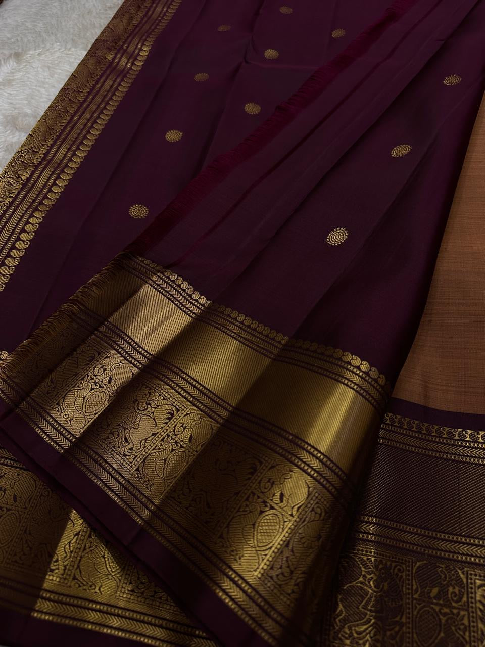 Pari is a graceful Kanchipuram pure silk saree in a serene copper-rose gold brown hue. Scattered peacock zari buttas . Framed by an antique-gold korvai border temple-inspired yali, annam, and floral medallions, finished with a deep wine-maroon Pallu