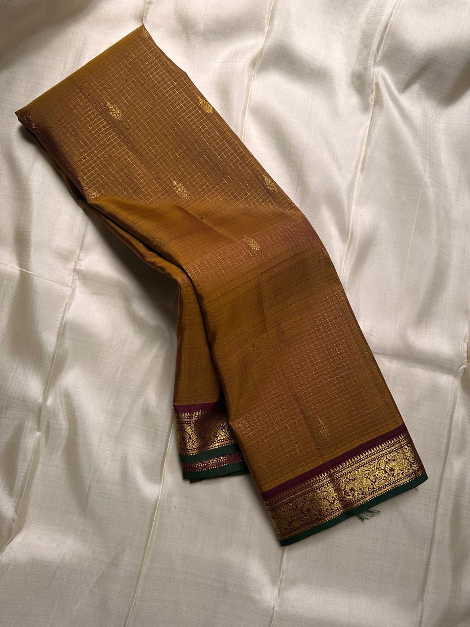 Amber Oosikattam ✨ – Pure Kanchipuram Silk Saree
Burnished Amber-Gold Body in Oosi Zari Kattam with Leaf Buttas
Deep Maroon Korvai Border with Green Selvedge & Elephant Motifs
Regal Maroon Pallu with Intricate Gold Zari Brocade
Silk Mark Certified |