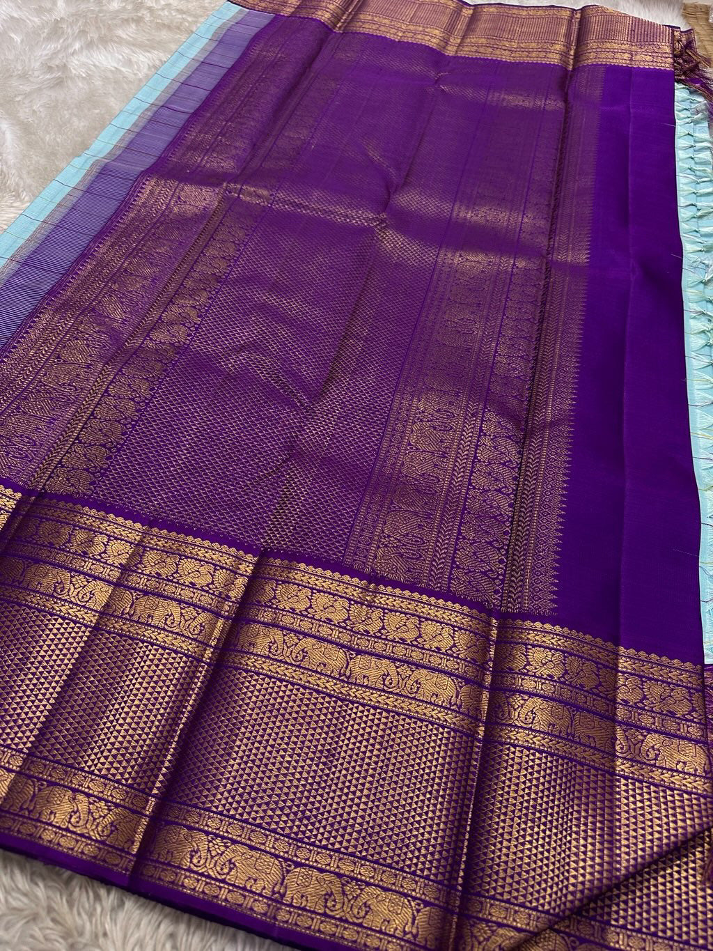 Aqua Amethyst zari kattam Pure Kanchipuram Silk Saree with blue Checks & Purple Border
Radiant sky-blue silk woven with delicate golden checks.
Grand purple korvai borders with elephant and floral motifs.
Silk Mark Certified, delivery in 2 weeks