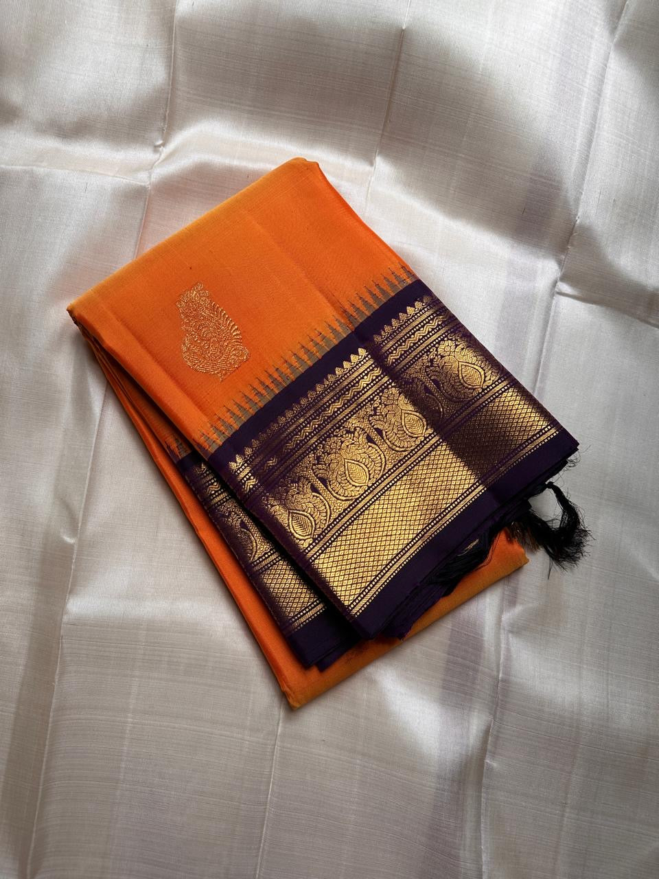 Pure Kanchipuram Silk Saree – Saffron-Orange Body with Gold Zari Paisley Buttas
Contrast Deep Purple Korvai Borders with Intricate Temple & Floral Motifs
Grand Purple Zari Pallu with Diagonal zariWeave . Silk mark , ships in 2 weeks