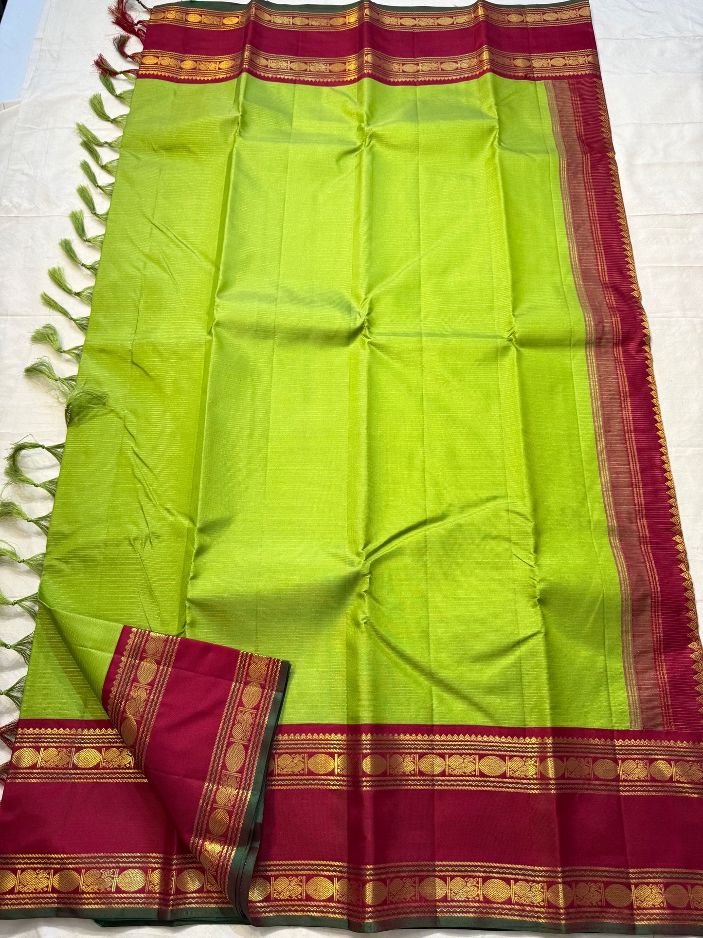 Maavilai Arakku Chakram — Korvai Kanchipuram Pure Silk
Parrot-green vaira-oosi body with soft pin-stripe sheen
Contrast arakku/rani border with gold chakram medallions & temple motifs
Arakku pallu with all-over coin-jaal; contrast blouse included